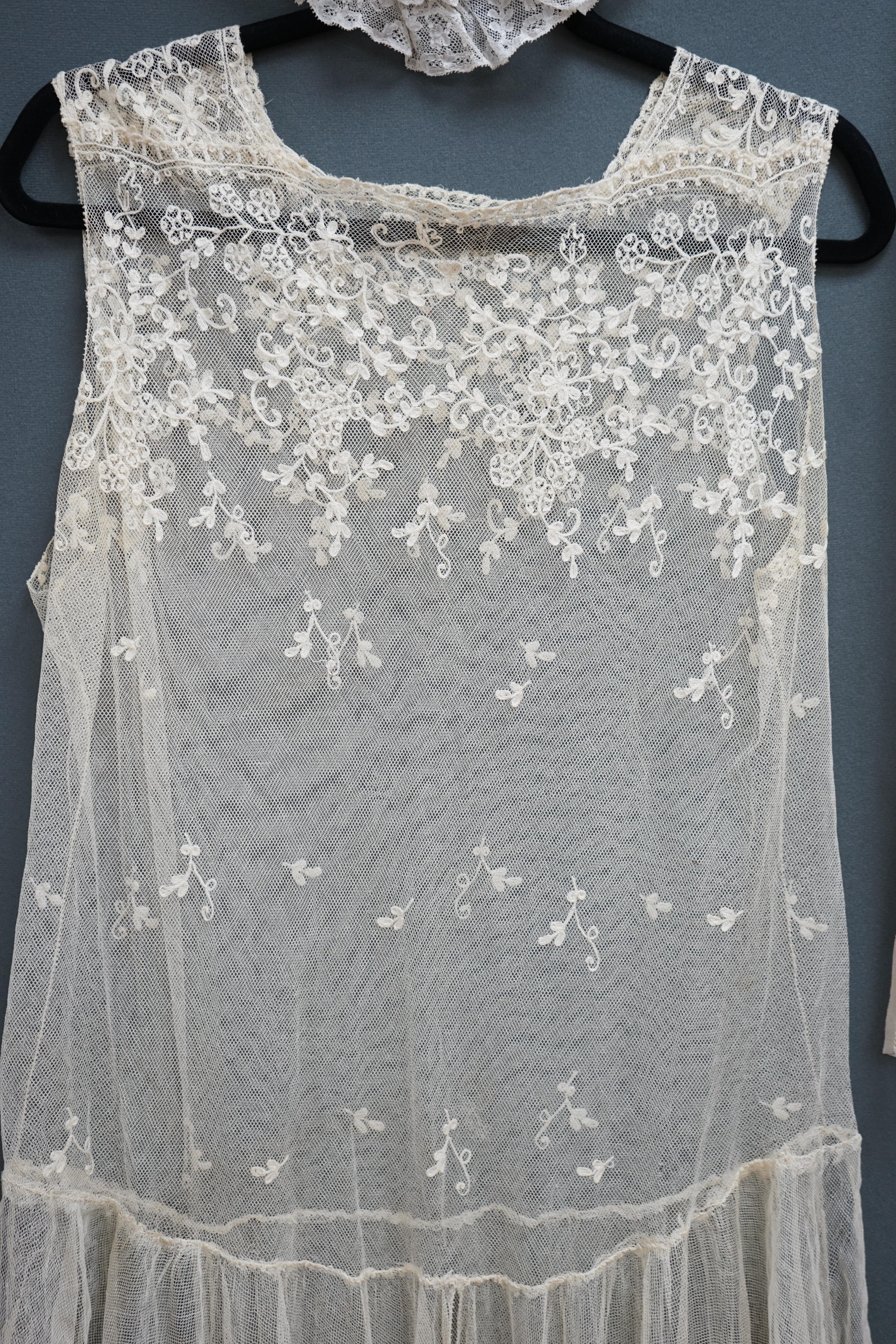 A 1920's cream net and needle run, lace wedding dress, together with a small silk net veil, and lace boudoir cap, the dress worked with a deep needle run bodice and skirt edge, with all over sprig motifs, designed with a